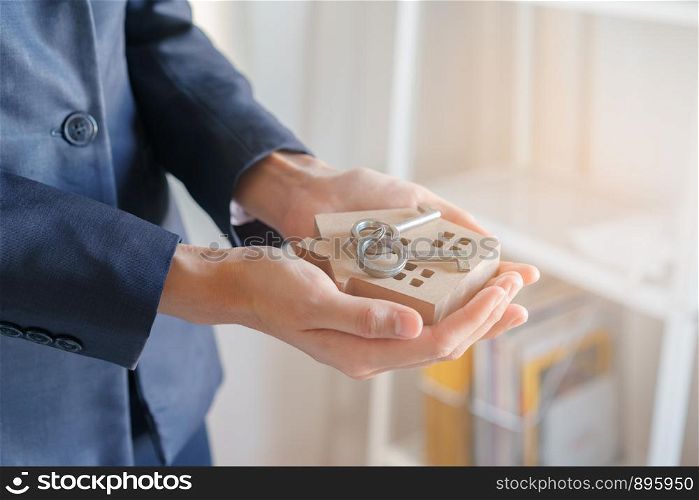 Close-up hand of Asian business woman are holding key and model houses in the office