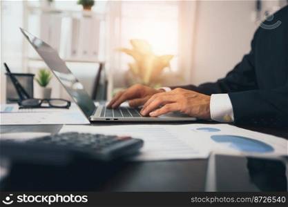 Close up hand of business man typing and working on laptop with  finance graph paper on table, manager check paperwork and analysis accounting in office, accounting and finance concept 