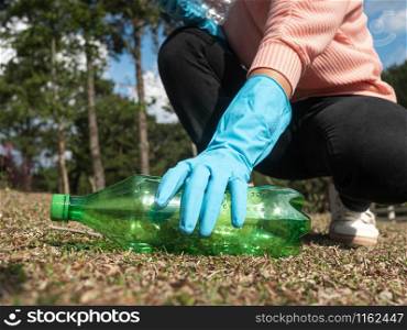 Close up hand of volunteer in gloves picks up a plastic bottle from the grass in the park. Concepts of save environment and stop plastic pollution.