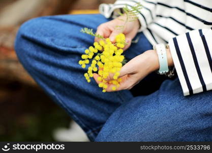 Close-up hand of young girl or woman holds yellow brunch of mimosa flowers outdoors. 8 march women&rsquo;s day concept. copy space.. Close-up hand of young girl or woman holds yellow brunch of mimosa flowers outdoors. 8 march women&rsquo;s day concept. copy space