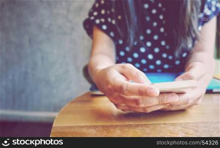 Close up hand of young woman using smartphone in home office or cafe with copy space, retro filter style