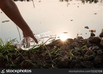 Close up Hand picking up a clear plastic bottle drop on the ground with polluted water background