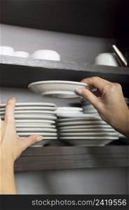 close up hand stacking white saucer shelf