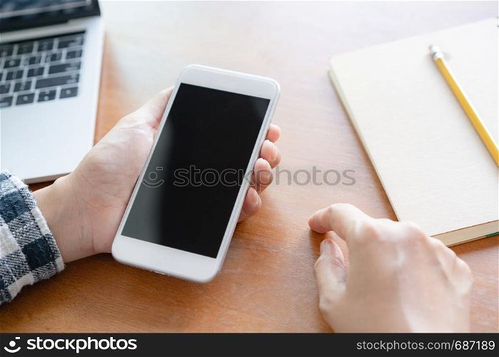 Close up hand using smartphone on desk background in office. On hand holding smartphone blank display.
