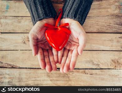 Close up hand woman holding and person red heart on wood table. Valentine background.