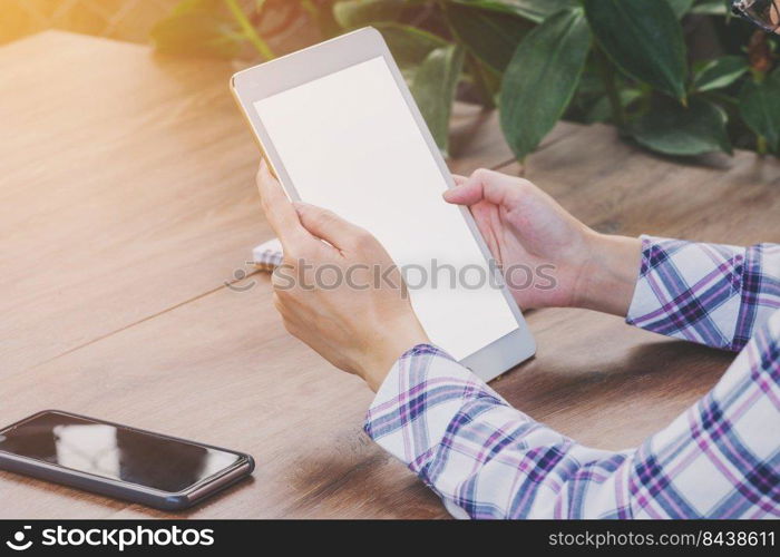 Close up hand woman holding tablet blank screen display on wood table with sunlight. Vintage toned.