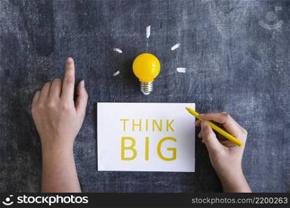 close up hand writing text think big white paper with yellow light bulb chalkboard