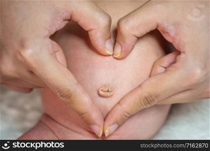 close up hands makes heart on belly of newborn baby
