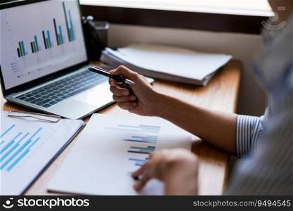 Close up hands of businessman reads document and pointing financial data on screen laptop with pen.