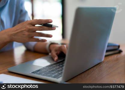 Close up hands of businesswoman holds pen to pointing on screen and typing data on laptop keyboard.