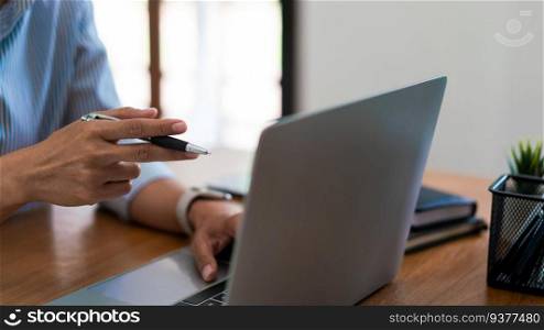 Close up hands of businesswoman holds pen to pointing on screen and typing data on laptop keyboard.