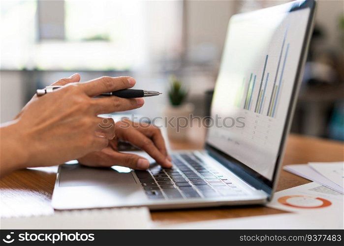 Close up hands of businesswoman holds pen to pointing on screen and typing data on laptop keyboard.
