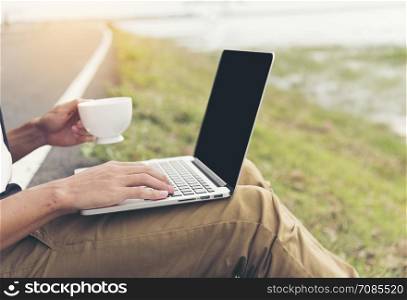 Close up hands of handsome man using laptop holding cup of coffee at outdoor cafe. Freelance working outdoor. Lifestyle new generation work as a freelance.