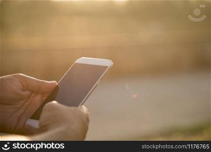 Close up hands of man using smart phone outdoor with the sunlight.