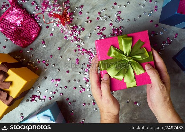Close up hands of parent giving a Christmas gift with colorful gift box and little star craft background . Cement texture desktop top view .