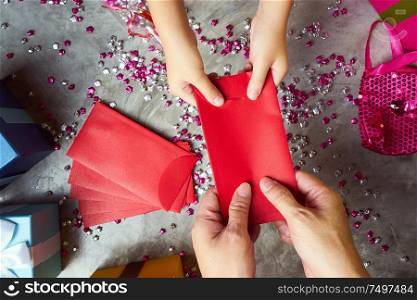 Close up hands of parent giving a red envelope or money red packet to child . Chinese new year and Lunar new year festival concept background . Top view .