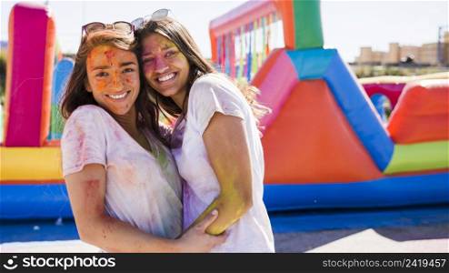 close up happy young women with holi color their face embracing
