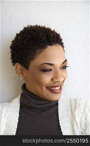 Close up head and shoulder of African-American woman standing against white wall smiling with head turned to side.