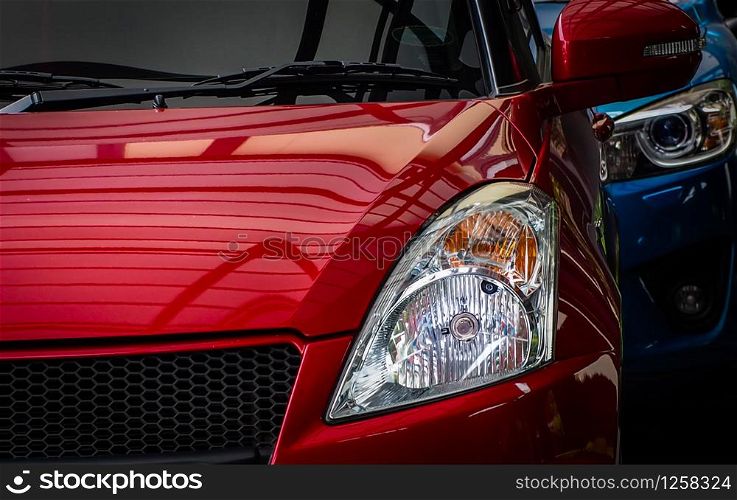 Close up headlamp light of red shiny SUV car parked on concrete parking lot of the hotel or shopping mall. Automotive industry concept. Electric or hybrid car technology. Car rental and dealership.