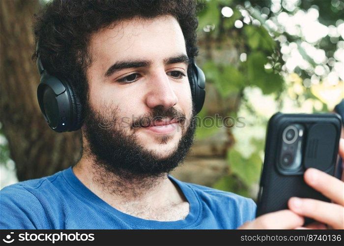 Close-up headshot of a young man wearing a blue t-shirt listening to modern music on his mobile phone with big wireless headphones