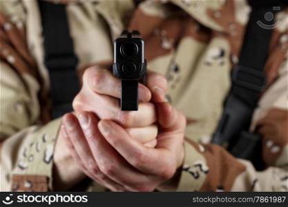 Close up horizontal image of pistol, pointing forward, with armed male soldier in background. Focus on front part of weapon with soldier blurred out.