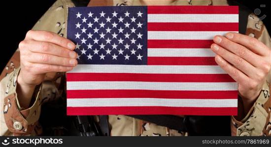 Close up horizontal image of United States of America flag with armed male soldier holding it while on black background.