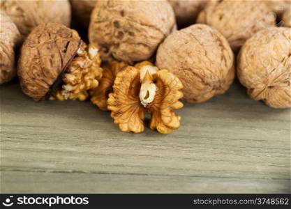 Close up horizontal photo of unshelled half of walnuts lying on faded wood with additional nuts both shelled and unshelled in background