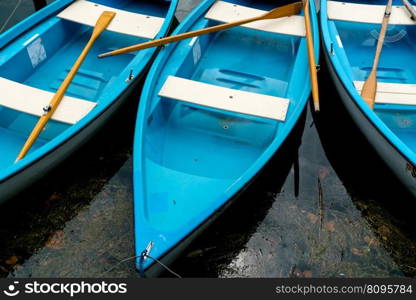 close up horizontal view of bright blue and white rowboats in dark lake water with brown wooden oars