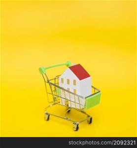 close up house model miniature shopping cart against yellow backdrop