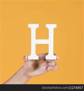 close up human hand holding up uppercase capital letter h yellow background