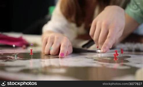 Close up human hands pointing travel destination on travel map with finger. Young couple planning summer vacation trip together on scratch travel map of the world. Map with pins showing location or aims. Tourism and planning vacation concept.