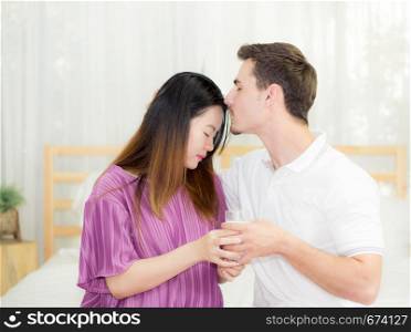 close up husband man kiss forehead woman belly sitting on the bedroom, couple wait the birth of child with a happy, family concept.