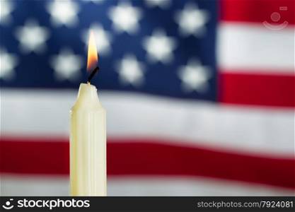 Close up image of a single white candle and glowing flame with United States of America flag in background. Fourth of July holiday concept.