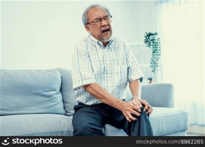 Close up image of an agonizing senior man with knee problem, pain, and ache while attempting to dispel on sofa by himself. Sickness in the elderly, medical services for the elderly. Close up image of an agonizing senior man with knee problem.