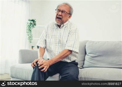 Close up image of an agonizing senior man with knee problem, pain, and ache while attempting to dispel on sofa by himself. Sickness in the elderly, medical services for the elderly. Close up image of an agonizing senior man with knee problem.