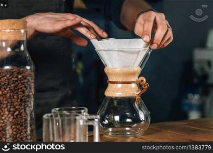Close up image of barista hands making filter coffee. Barista with tattooed arms wearing dark uniform.