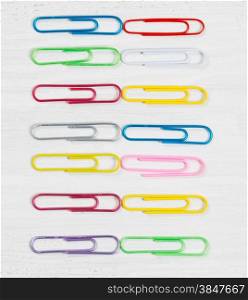 Close up image of colorful paper clips on white wood.
