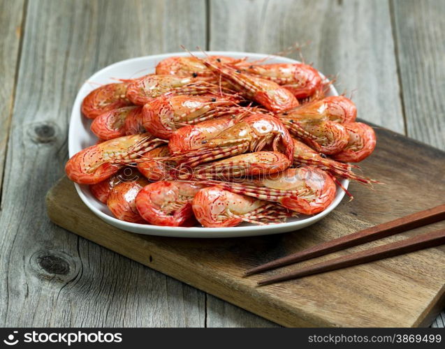 Close up image of cooked shrimp in white plate on top of server with rustic wood underneath.