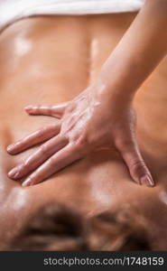 Close up image of physiotherapist massaging female patient with injured back muscle. Sports injury treatment.