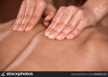 Close up image of physiotherapist massaging female patient with injured back muscle. Sports injury treatment.