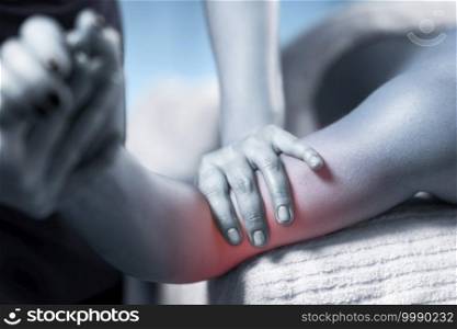 Close up image of physiotherapist massaging female patient with injured elbow. Blue colored image. Red accent on the arm. Sports injury treatment.