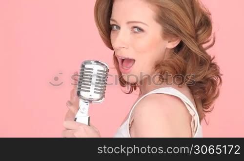 Close-up image of the face of a female singer with her mouth open in song holding a microscope.
