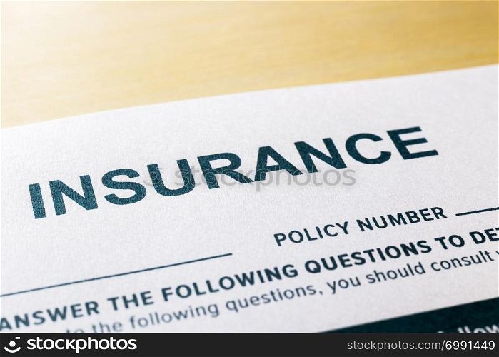 Close up image, selective focus on word INSURNCE, questionnaire and application form on wooden desk background. Healthcare, security, personal safety plan and business invesment concepts.