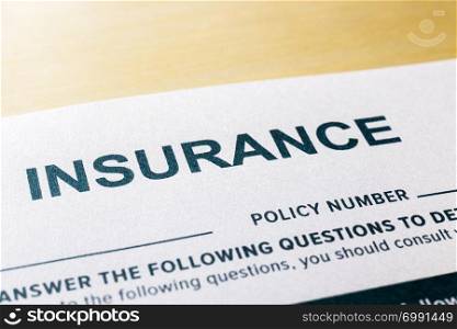 Close up image, selective focus on word INSURNCE, questionnaire and application form on wooden desk background. Healthcare, security, personal safety plan and business invesment concepts.