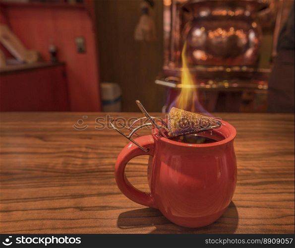 Close-up image with a cup of mulled wine, on top of which stands a burning cone of brown sugar, previously dipped in a lot of rum. This is a traditional german Christmas drink, called  Feuerzangentasse , in translation Fire Cup.