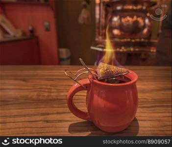 Close-up image with a cup of mulled wine, on top of which stands a burning cone of brown sugar, previously dipped in a lot of rum. This is a traditional german Christmas drink, called  Feuerzangentasse , in translation Fire Cup.