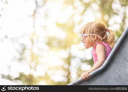 Close-up image with a little girl having fun on a slide from a playground, on a sunny day.