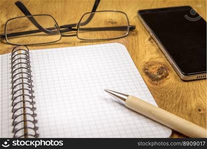 Close-up image with an opened graph, spiral notebook, eyeglasses, pen and phone on a vintage, wooden table. Perfect as a frame or background.