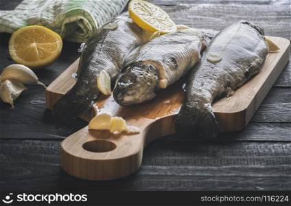 Close-up image with fresh trout displayed on a wooden cutting board, seasoned with garlic and lemon slices, on a rustic wooden table, on a sunny day.