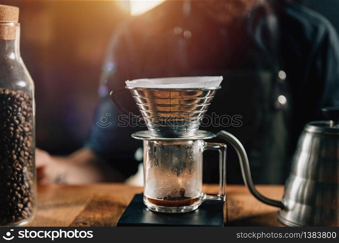 Close up Kalita Wave Dripper on black digital scale, wooden table. Tools and equipment for making Drip Brew coffee. Barista with tattooed arms wearing dark uniform.